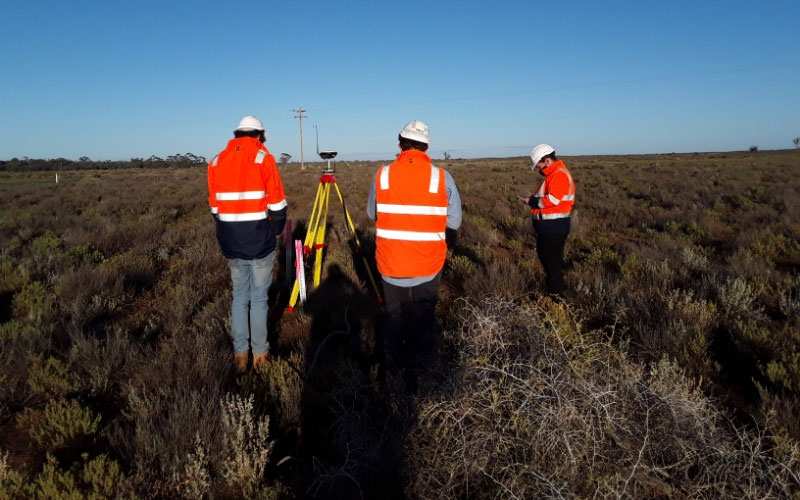 three men surveyour in orange vests standing in a field